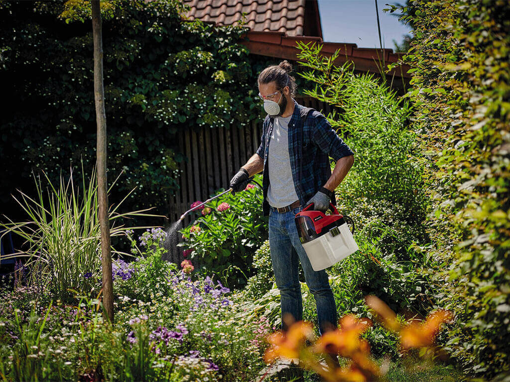 A man waters his plants with the help of a cordless pressure sprayer from Einhell.