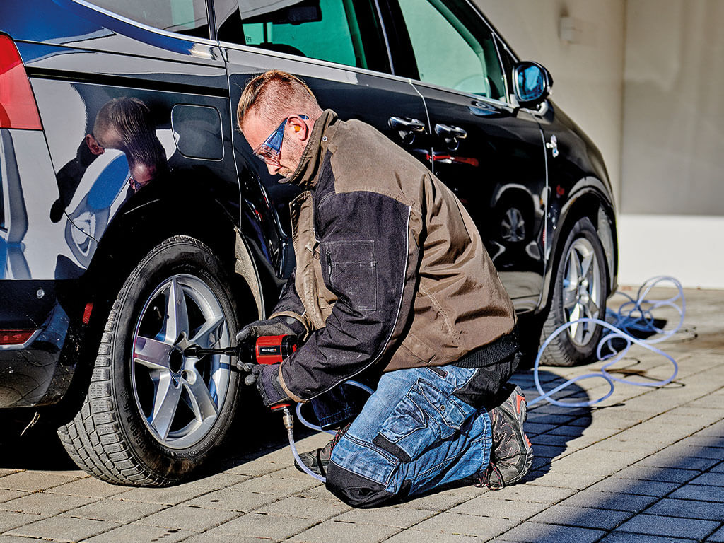 A man loosens the wheel nuts on his car tyre with a pneumatic impact wrench from Einhell.